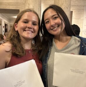 Ella and Kat holding up white envelopes inside Kirby Hall.